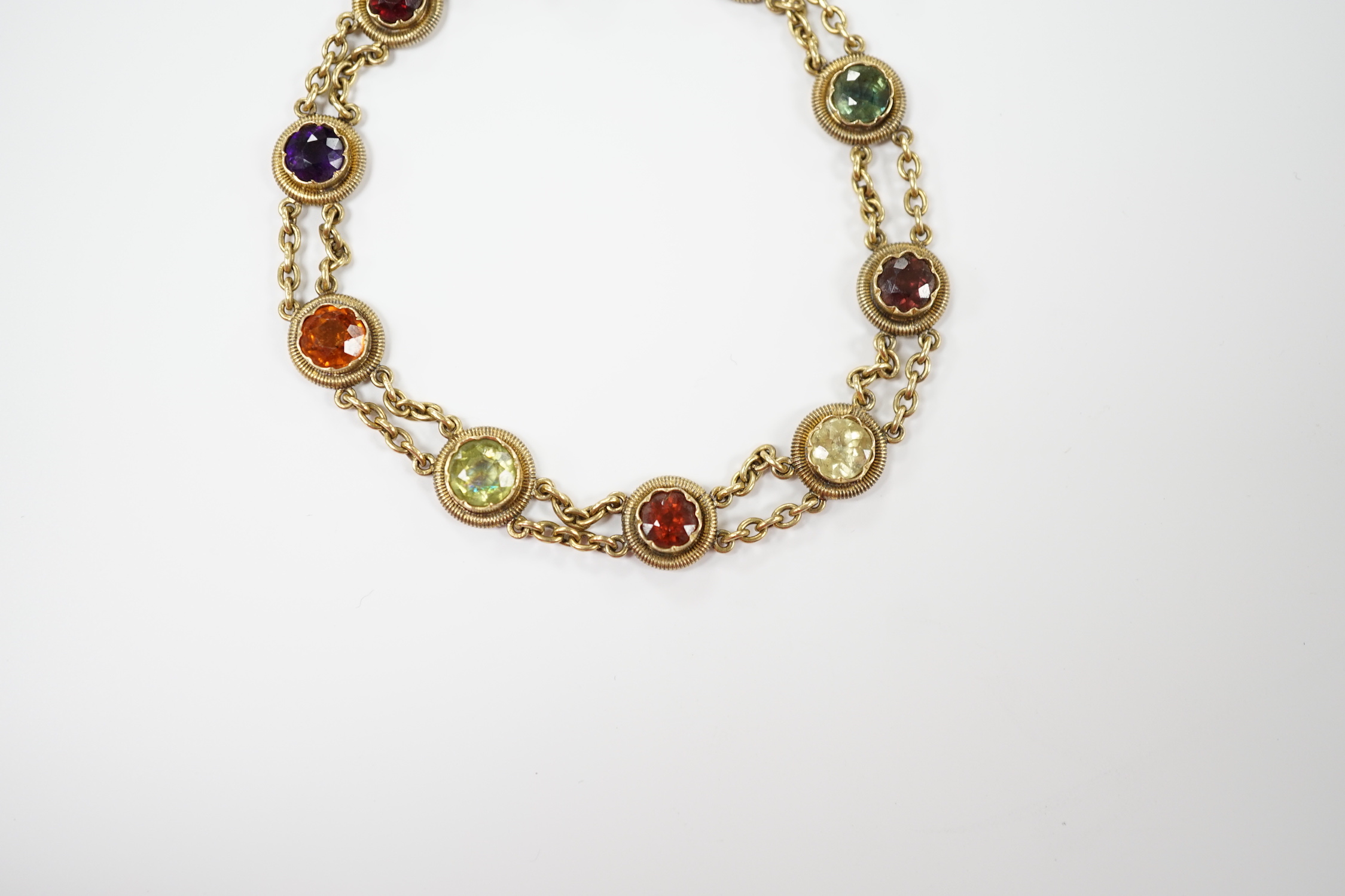 An early 20th century yellow metal (stamped 15 and also 9??) and ten stone multi gem set chain link bracelet, 16cm, gross weight 14.6 grams, the stones include amethyst, hessonite garnet and tourmaline.